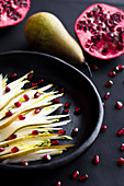 Pear and endive salad with pomegranate seeds in a black plate on black background