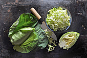 Pointed cabbage, whole, halved and sliced, in a ceramic bowl with a knife on a black baking tray