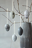 Easter eggs hand-painted in shades of grey hanging from twigs
