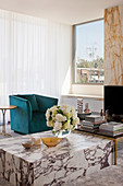 Bouquet of flowers on marble coffee table, turquoise armchair in front of window in living room