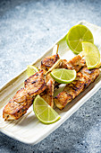 Grilled chicken breast skewers with lime on a light plate and light travertine marble table