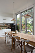 Long wooden table and chairs next to balcony doors in white, open-plan kitchen