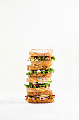Four stacked sandwiches with tomatoes, chicken and corned beef