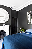 Double bed with dark blue bedspread, fireplace and mirror in the bedroom with black walls