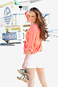 A young woman on a beach wearing a salmon pink blouse and a pair of shorts