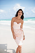 A young, long-haired woman on a lounger on a beach wearing a light, strapless dress