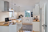 weiße Küche mit halbrunder Frühstückstheke an Küchenzeile und Barhockern in umgebauter Molkerei