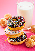 Stack of chocolate and vanilla glazed donuts with sprinkles and donut holes with a glass of milk
