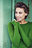 Kurzhaarige Frau in grünem Pulli vor grüner Hintergrund