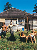 Junge Frau in schwarzem Maxikleid und junge Männer in Badeshorts im Garten