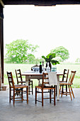 Wooden chairs around table on concrete floor with view of green garden