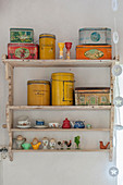 Brightly coloured tins and doll's crockery on old wall-mounted shelves