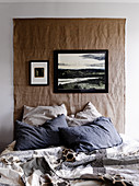 Wall-hanging made from coarse fabric above bed with patchwork quilt