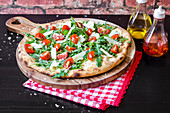 Pizza made with a sourdough base, fresh rocket leaves, cherry tomatoes and parmigiano cheese on a wooden board