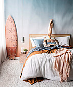 Pastel-colored bedroom, young woman on double bed, pendant lamp and surfboard next to it