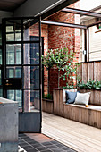 Eingebaute Sitzbank und Grünpflanzen auf Terrasse mit Backsteinmauer und Industrietür