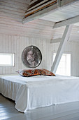 Bed in attic bedroom with white wooden walls and exposed roof beams