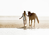 Woman and horse walking side-by-side on beach