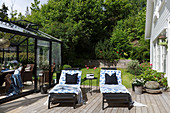 Two loungers on sunny wooden deck between conservatory and house