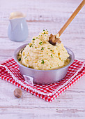 Homemade mashed potatoes in a metal bowl with a wooden masher
