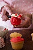 A cook decorating cupcakes with red icing