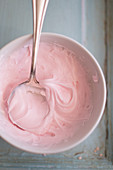 Pink frosting in a cup with a spoon