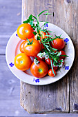 Frische Tomaten mit Estragon- und Oreganozweigen auf Teller (Aufsicht)