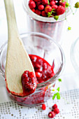 Wild strawberry jam in a glass and on a wooden spoon (close up)