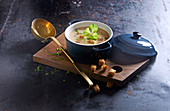 Potato soup with croutons in a ceramic pot on a wooden board
