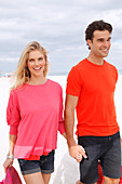 Blonde Frau in rosa Bluse und brünetter Mann in orangefarbenem T-Shirt am Strand