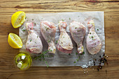 Raw marinated chicken legs on a paper with ingredients