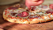 Salami pizza being sliced with a pizza cutter