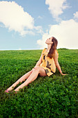 A young woman sitting in a field wearing a summer dress