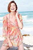 A red-haired woman by the sea wearing a beach dress
