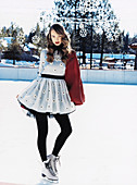 Junge Frau in elegantem Retrokleid und schwarzer Strumpfhose mit Schlittschuhen auf Eis