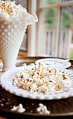 Popcorn sprinkled with sea salt in an antique white dish, with white plates with sea salt and extra popcorn pictured below