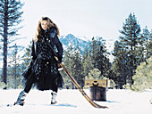 A young woman in the snow with an ice hockey stick wearing a blue dress and a coat