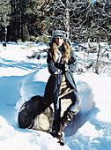 A young woman on a log in the snow wearing a faux fur hat