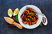 Grilled prawns in white plate with lemon, soy sauce and spices on wooden board over dark vintage stone background