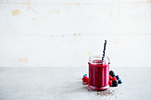 Tasty berry smoothie with fresh berries and straw in glass jar, white wooden wall background