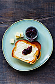 Top view of whole grain bread toasts with butter and fruit jam for traditional breakfast on wooden background