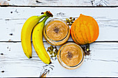 Glass jars of healthy pumpkin banana smoothie with chia seed and ingredients on white grunge wooden background