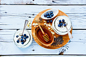 Mason jars of breakfast yogurt with chia seeds, honey and fresh blueberries on white grunge wooden background