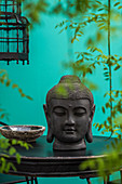 Head of Buddha on black table and leafy tendrils against turquoise wall