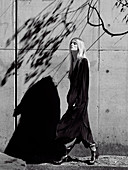 A young woman wearing a long, black cardigan against a concrete wall (black-and-white shot)