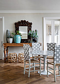 Stühle mit gepunkteter Rückenlehne an rundem Esstisch, dahinter Holzrahmenspiegel und Blumentöpfe auf Konsolentisch