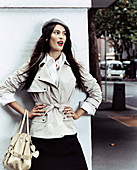 A dark-haired woman wearing a beret, a light trench coat and a black skirt