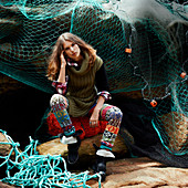 A brunette woman wearing a long, knitted jumper and leggings in front of a fishing net