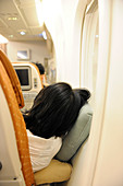 Passenger sleeping in economy class airline cabin