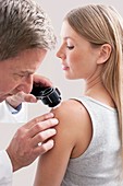 Doctor examining mole on young woman's shoulder